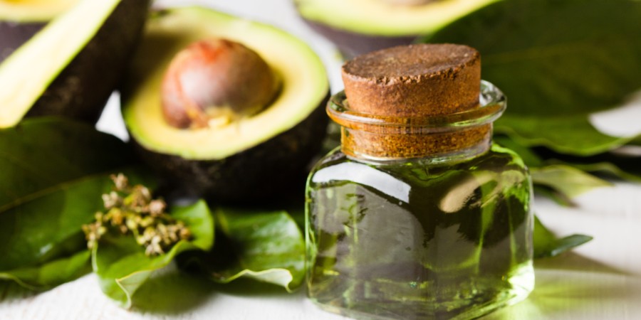 Avocado oil in a jar with avocado halves in the background