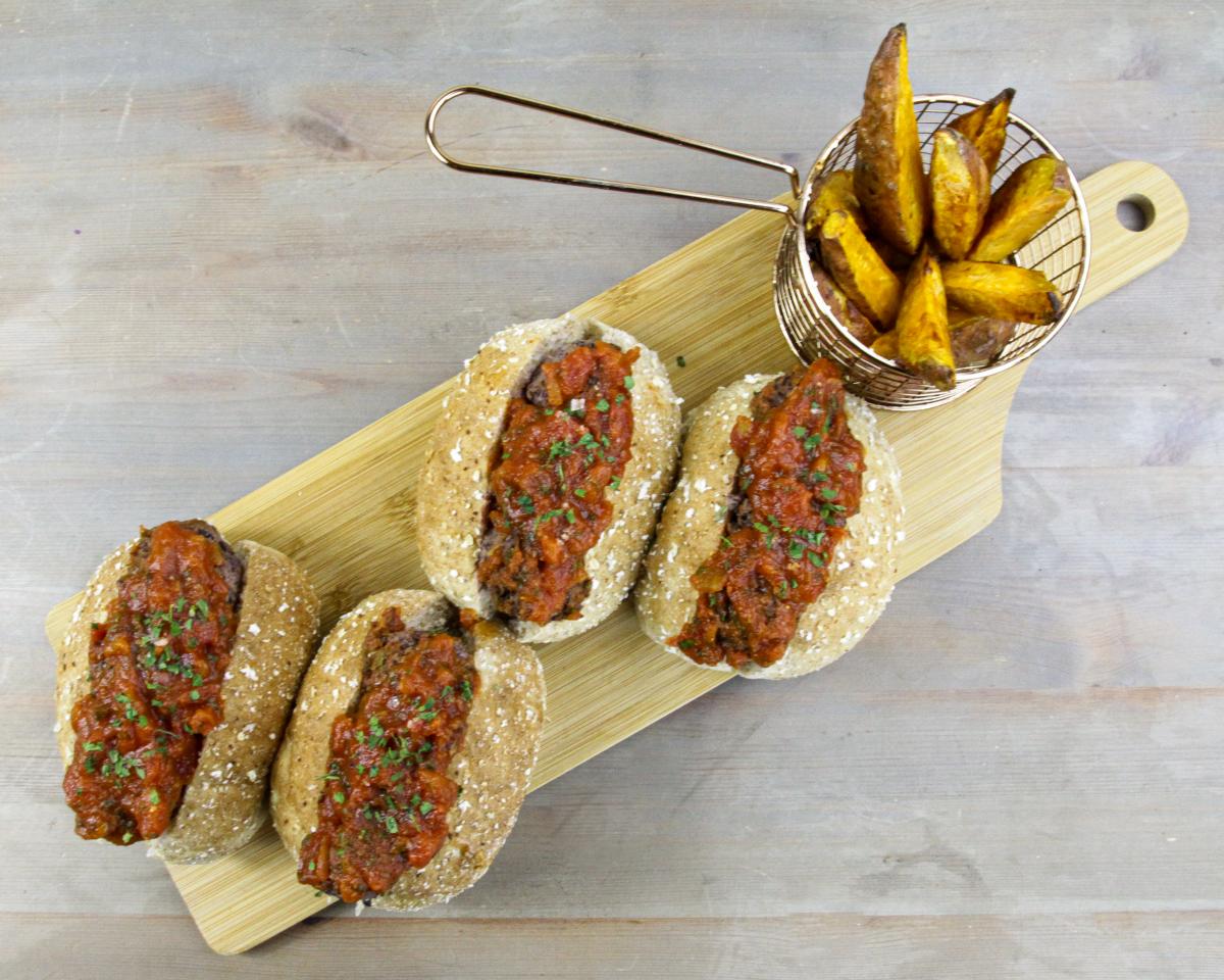 four vegan black beanball marinara subs and a small metal basket of wedges on a wooden board against a grey background