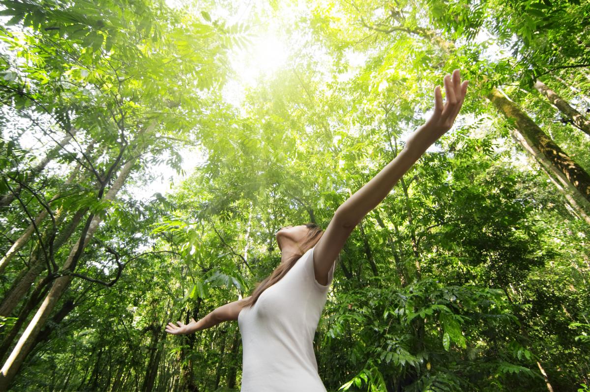 young woman standing in forest with arms raised