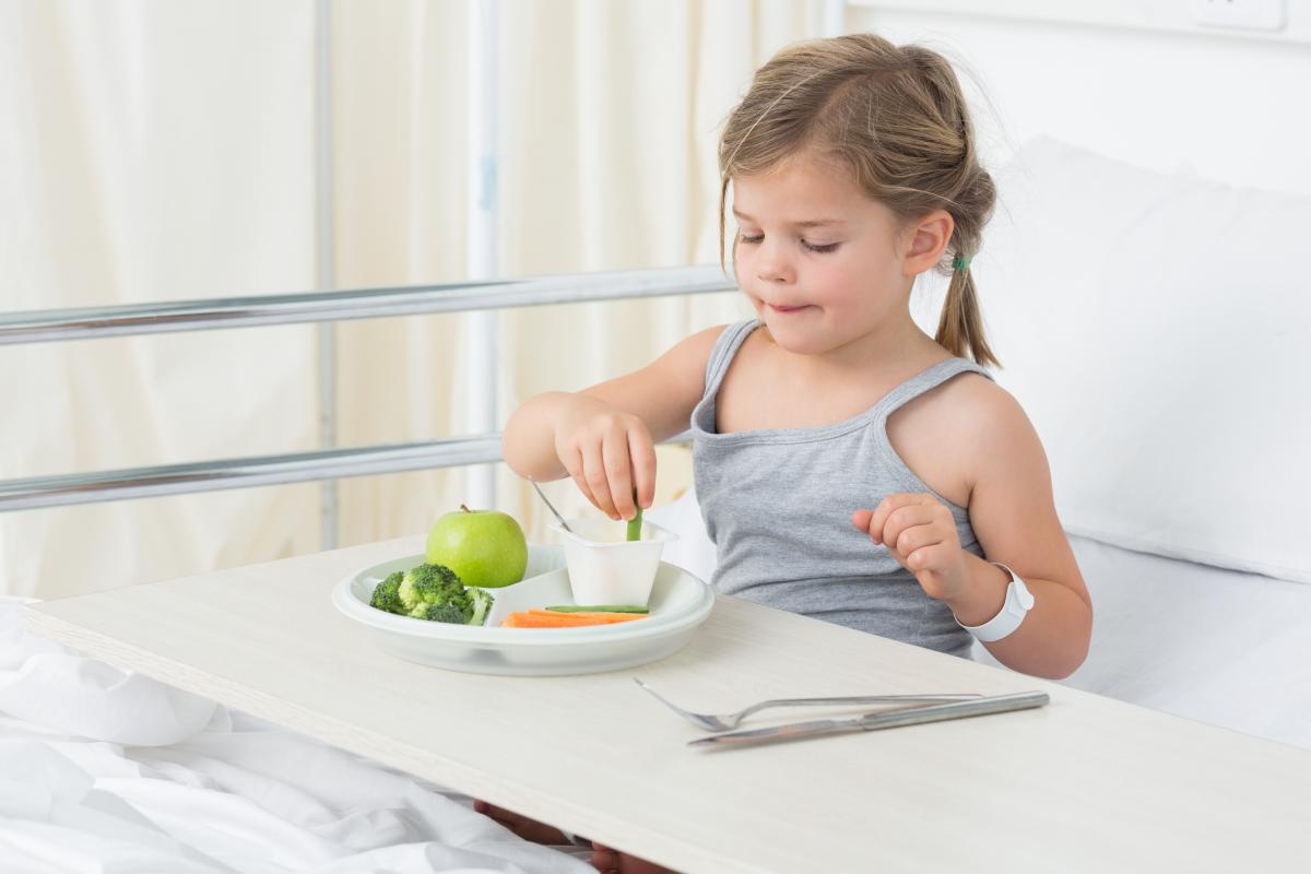 Child in hospital bed eating veggies