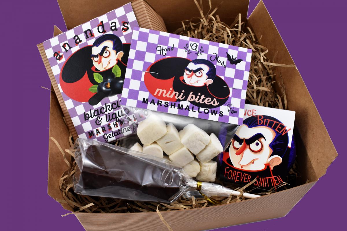 Halloween gift box on a purple background containing chocolate and marshmallows
