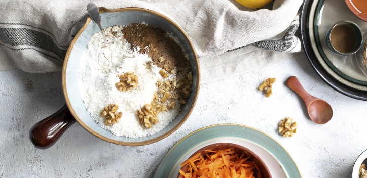 Flour, cinnamon and walnuts in a mixing bowl next to a bowl of grated carrots.