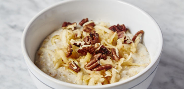 A bowl of porridge with apple and pecans sprinkled on top.