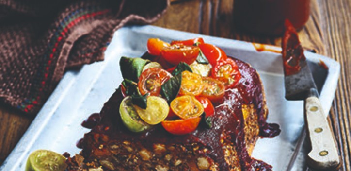 Vegan BBQ meatloaf topped with halfed cherrie tomatoes and served in a shallow square dish.