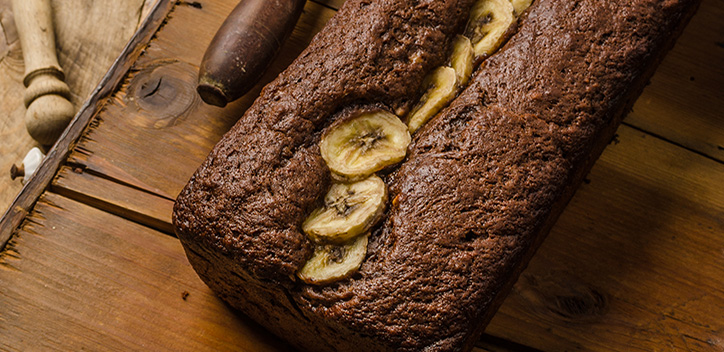 A loaf of banana bread topped with banana slices served on a wooden board.