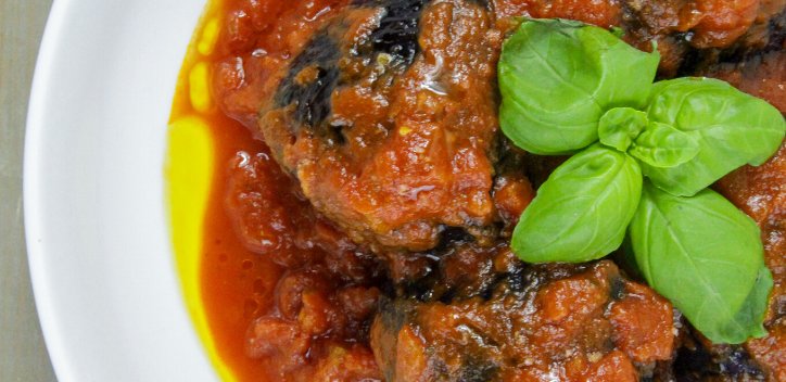 Stuffed cabbage parcels in a tomato and chilli sauce served on a round plate.