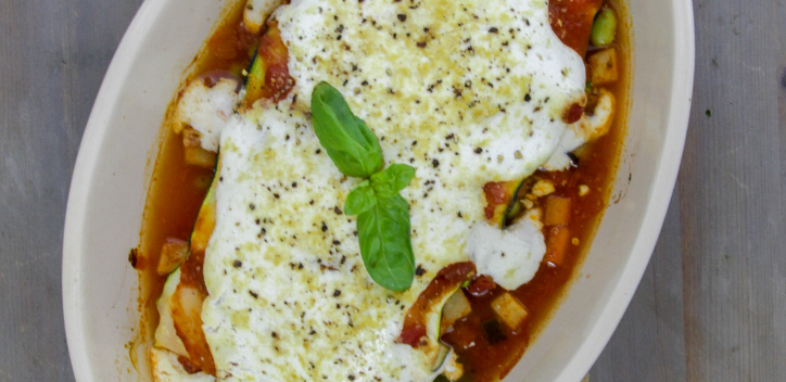 Vegan carrot and courgette cannelloni in a white oval oven dish on a wooden board against a grey background