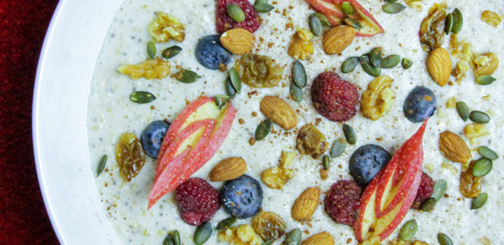 Vegan breakfast porridge with nuts and fruit in a white bowl on a red background.