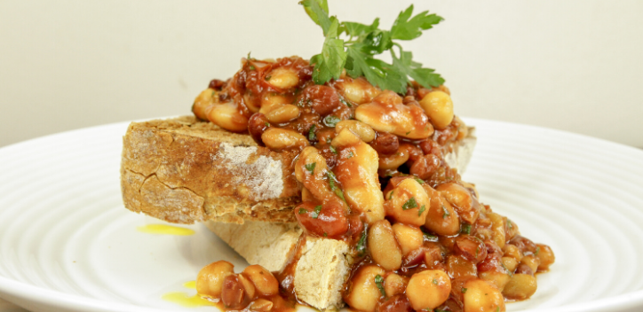 Crusty bread topped with mixed beans in a barbeque sauce, served on a round plate.