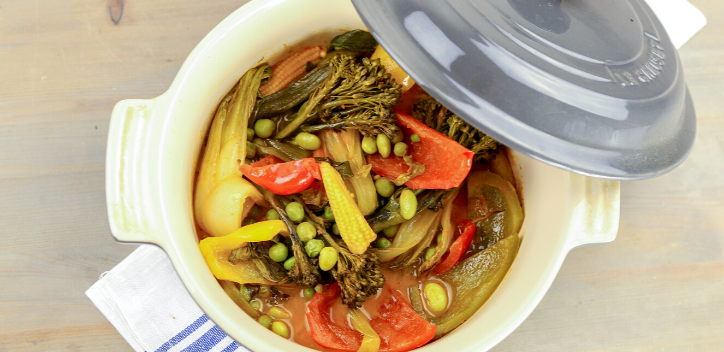 A deep baking dish filled with broccoli, peppers, sweetcorn, pak choi, spring onions and edamame beans with the lid resting on the side. 