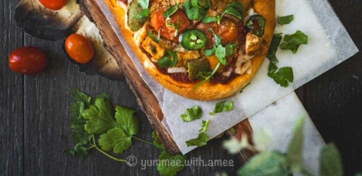 Tikka masala naan pizza surrounded by herbs and tomatoes. 