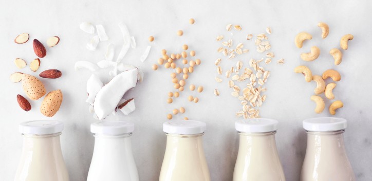 Vegan, plant based, non dairy milk. Variety in milk bottles with ingredients. Above view over a white marble background.