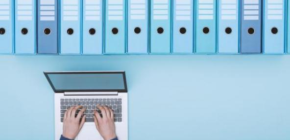 Person typing on a laptop below binder folders