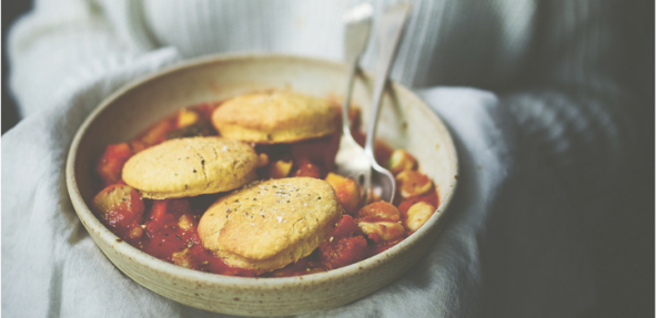A bowl of mixed vegetable stew topped with three scone dumplings 
