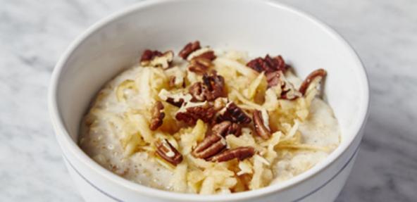A bowl of porridge with apple and pecans sprinkled on top.