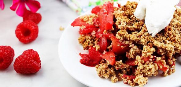 A plate of apple and raspberry crumble with extra raspberries and cream on top.  Additional rasperies to the leftside of the plate.