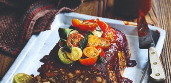 Vegan BBQ meatloaf topped with halfed cherrie tomatoes and served in a shallow square dish.