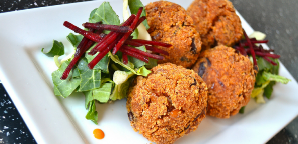 Four arancini balls served with a leafy beetroot salad on a square plate dotted with a dipping sauce.