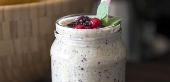 A jar filled with banana and berries smoothly topped with berries and mint leaf.