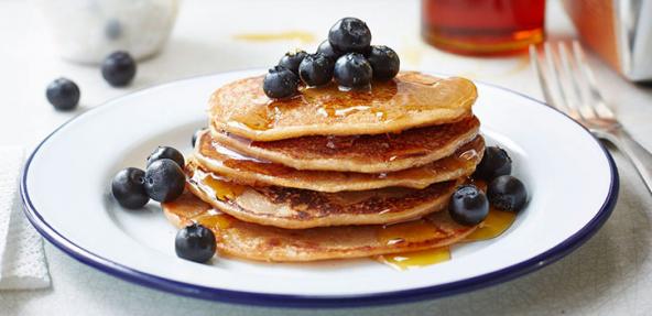 A stack of banana pancakes topped with blackberries, served on a circular plate.