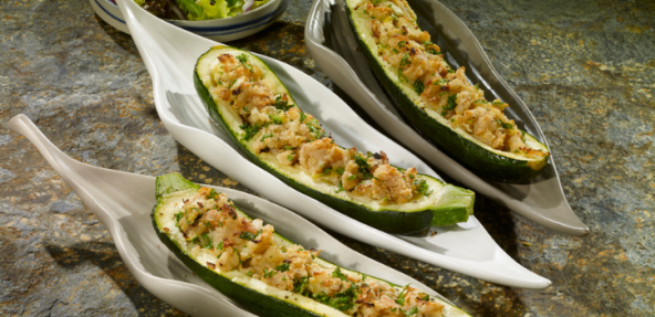 Three leaf shaped shallow bowls filled with half courgettes that are stuffed with almonds
