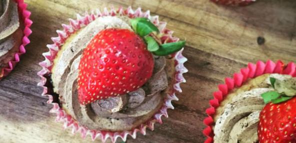 A selection of berry muffins topped with berry icing and strawberries.