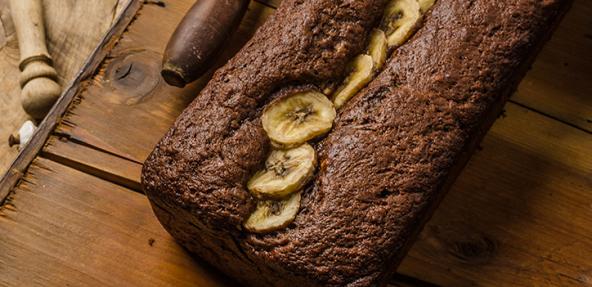 A loaf of banana bread topped with banana slices served on a wooden board.