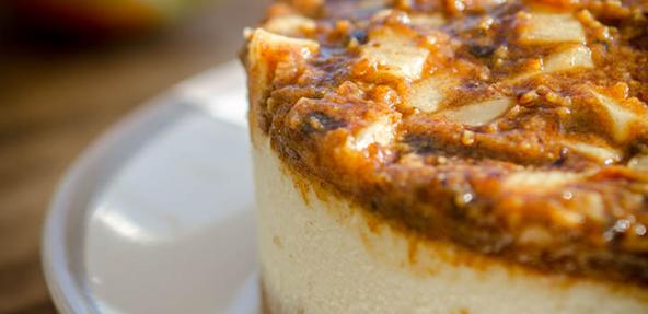 A zoom in of a cheescake on a plate, topped with apples and caramel.