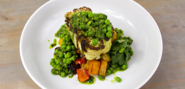 Vegan cauliflower steaks with chimichurri peas on a white plate against a grey background