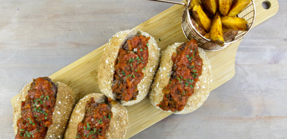 A selection of bread rolls filled with black bean marina sauce next to a side of potato wedges, served on a wooden platter.