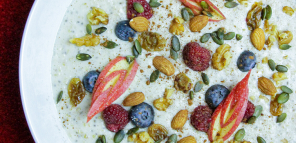 Vegan breakfast porridge with nuts and fruit in a white bowl on a red background.