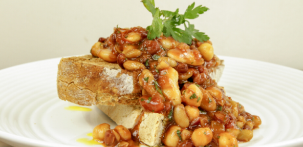 Crusty bread topped with mixed beans in a barbeque sauce, served on a round plate.