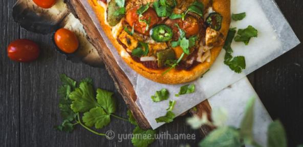 Tikka masala naan pizza surrounded by herbs and tomatoes. 