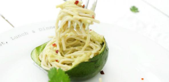 Half an avocado on a plate filled with creamy spaghetti, partly raised and twisted around a fork.  