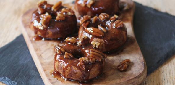 Four banana donuts topped with caramel and walnuts, served on a wooden board