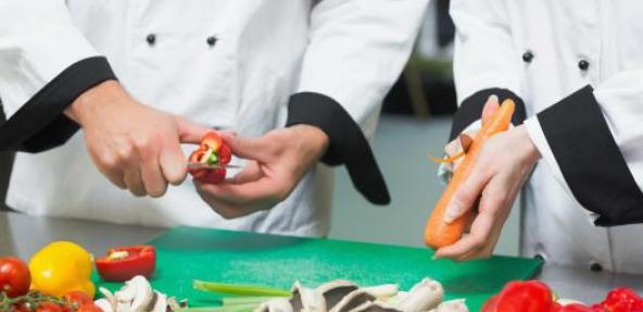 Two chefs cutting fruit and vegetables on chopping board