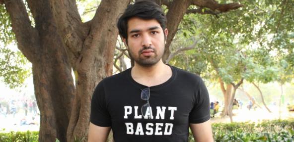 Image if Ishaan outside wearing a plant based t-shirt, holding a laptop reading 'but it is important to see' written on it.