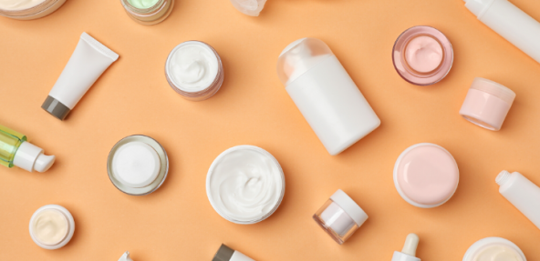 Plain cosmetics pots containing product, scattered across a peach coloured background.