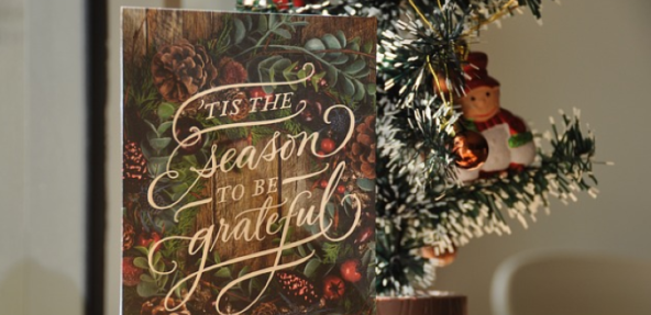 A Christmas card on a table with a miniature Christmas tree behind