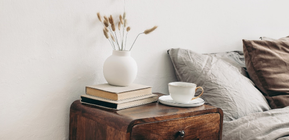 bedside table with books, tea cup and saucer and pot next to bed in a vegan home