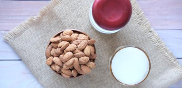 plant milk in a glass next to a bowl of almonds