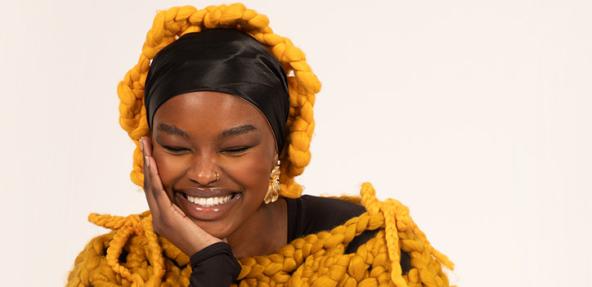 A woman smiling with her hand on her face, wearing Shone knitwear