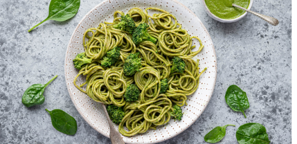 photograph of spinach pesto pasta on a dish surrounded by spinach leaves
