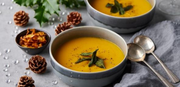 carrot soup in a bowl surrounded by pine cones and holly 