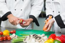 Two chefs cutting fruit and vegetables on chopping board