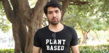 Image if Ishaan outside wearing a plant based t-shirt, holding a laptop reading 'but it is important to see' written on it.