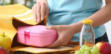 Woman packing fresh meal into lunch box bag in kitchen