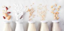 Vegan, plant based, non dairy milk. Variety in milk bottles with ingredients. Above view over a white marble background.