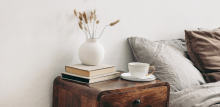 bedside table with books, tea cup and saucer and pot next to bed in a vegan home