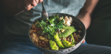 Healthy dinner or lunch. Person in t-shirt and jeans eating vegan superbowl or Buddha bowl with hummus, vegetable, salad, beans, couscous and avocado